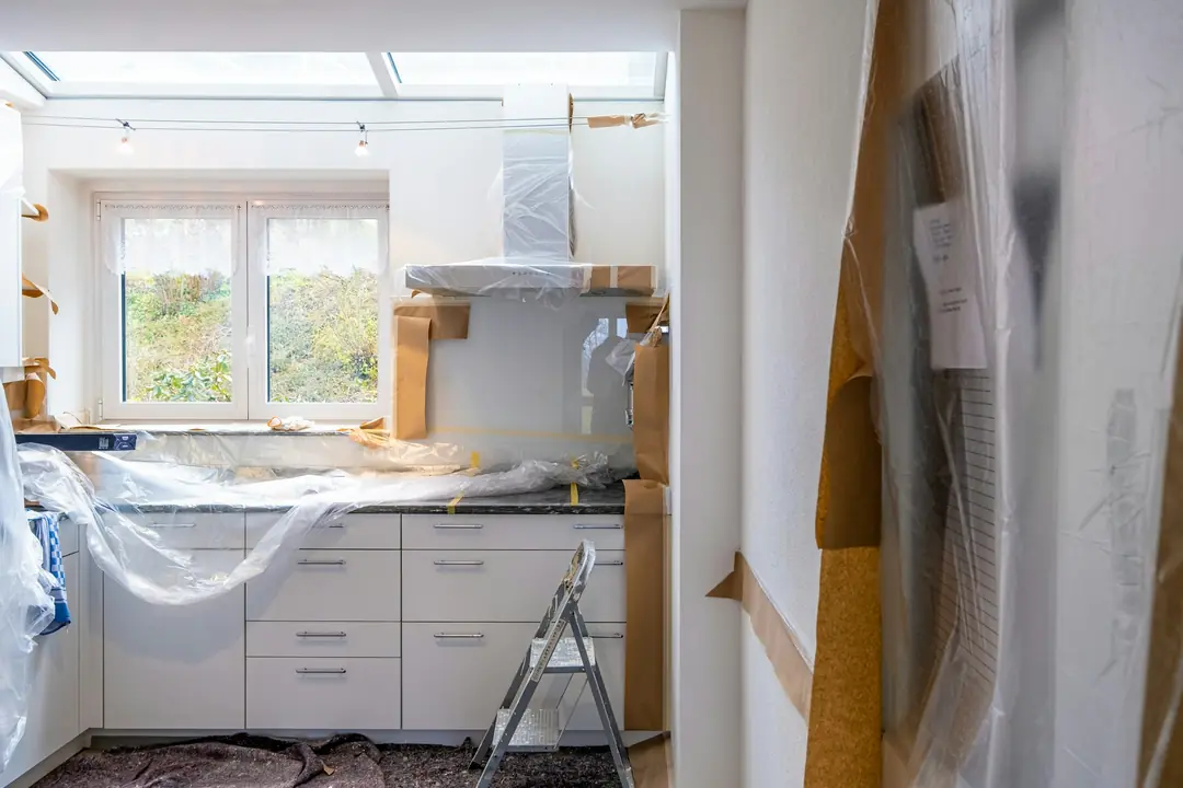A kitchen mid-renovation with white cabinets wrapped in protective plastic
