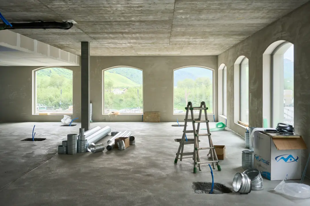 A large stripped room with arched windows, a ladder and materials on the floor