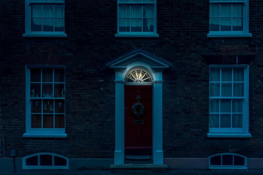 A red front door in a brick facade, lit from inside in the evening
